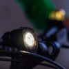 WOOM BEAM velosipēda lukturis melnā krāsā ar ieslēgtu priekšējo gaismu uz velosipēda stūres