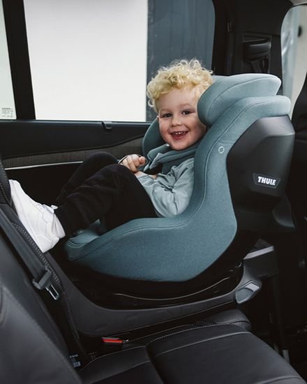 Zils bērnu autokrēsliņš ar sānu aizsardzību, kurā sēž smaidīgs mazulis automašīnā