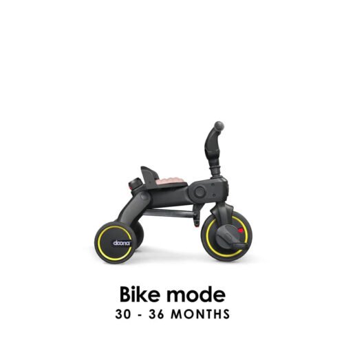 Doona Liki Trike S3 salokāms trīsritenis, melns ar rozā sēdekli un dzeltenām apmalēm, braukšanas režīmā