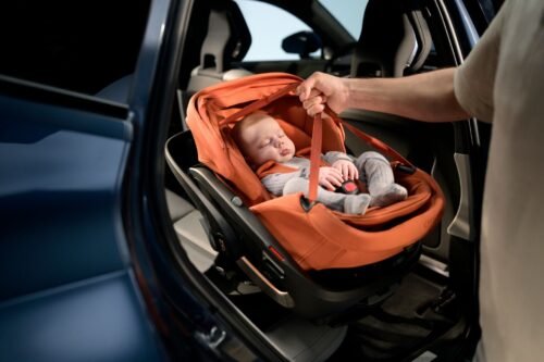 Oranžs Maxi-Cosi autokrēsliņš ar guļošu mazuli automašīnā