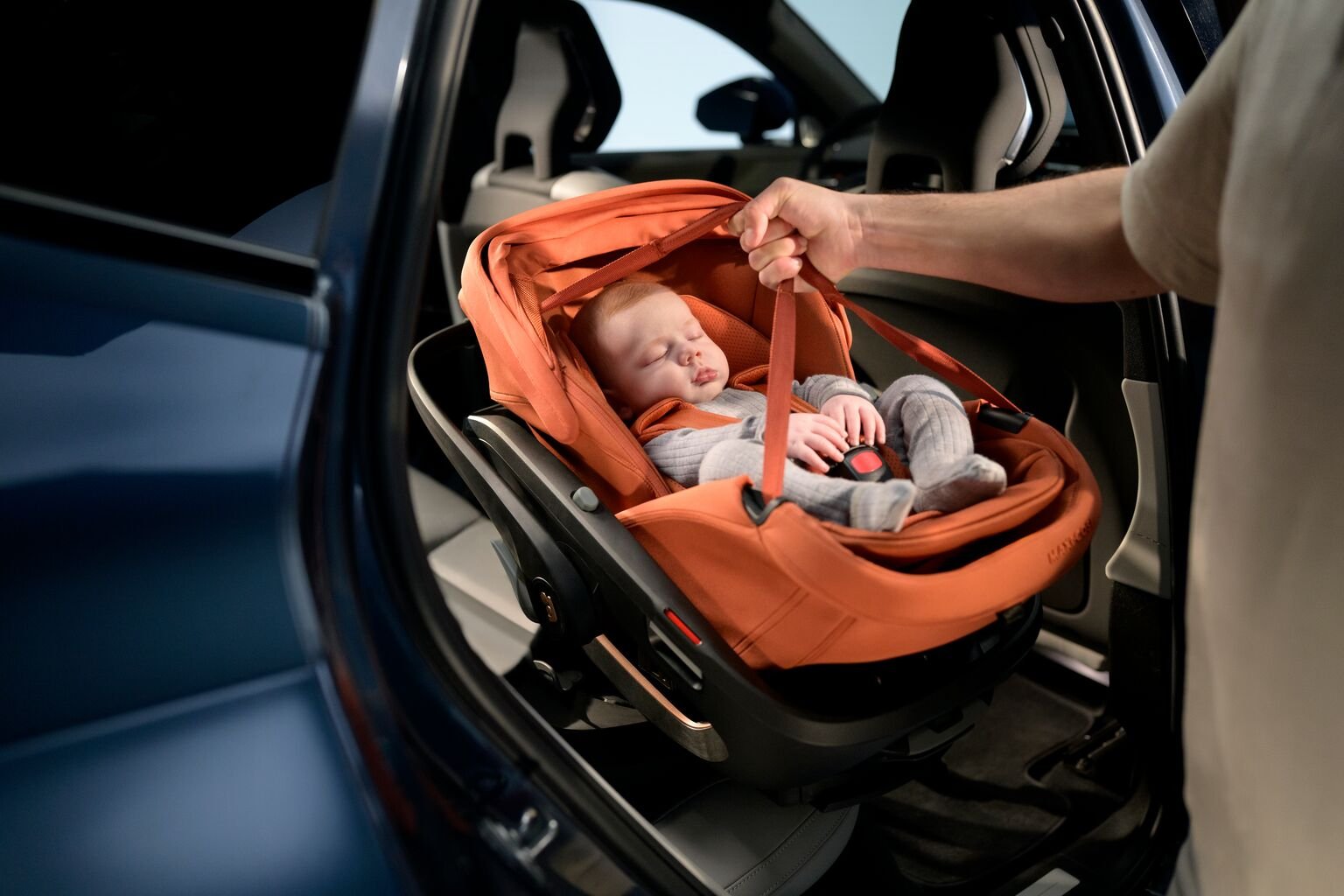 Oranžs Maxi-Cosi zīdaiņu autokrēsliņš automašīnā ar guļošu mazuli un piesprādzējumu
